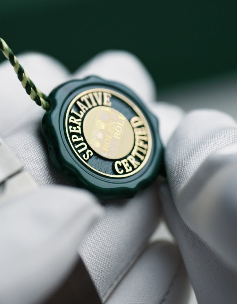 close up photo of two gloved hands holding a Rolex watch with a Superlative Certified seal
