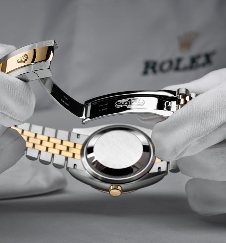 Two gloved hands holding a Rolex Watch